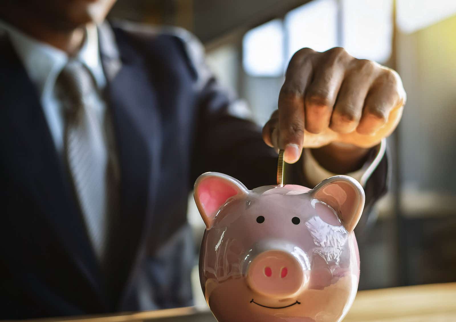 A businessman puts coins into a piggy bank.