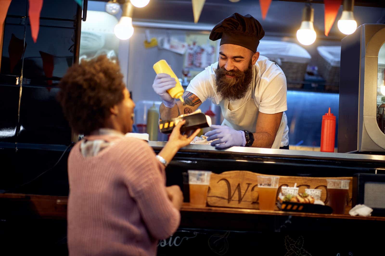 Street food vendor hands over hotdog to laughing customer.