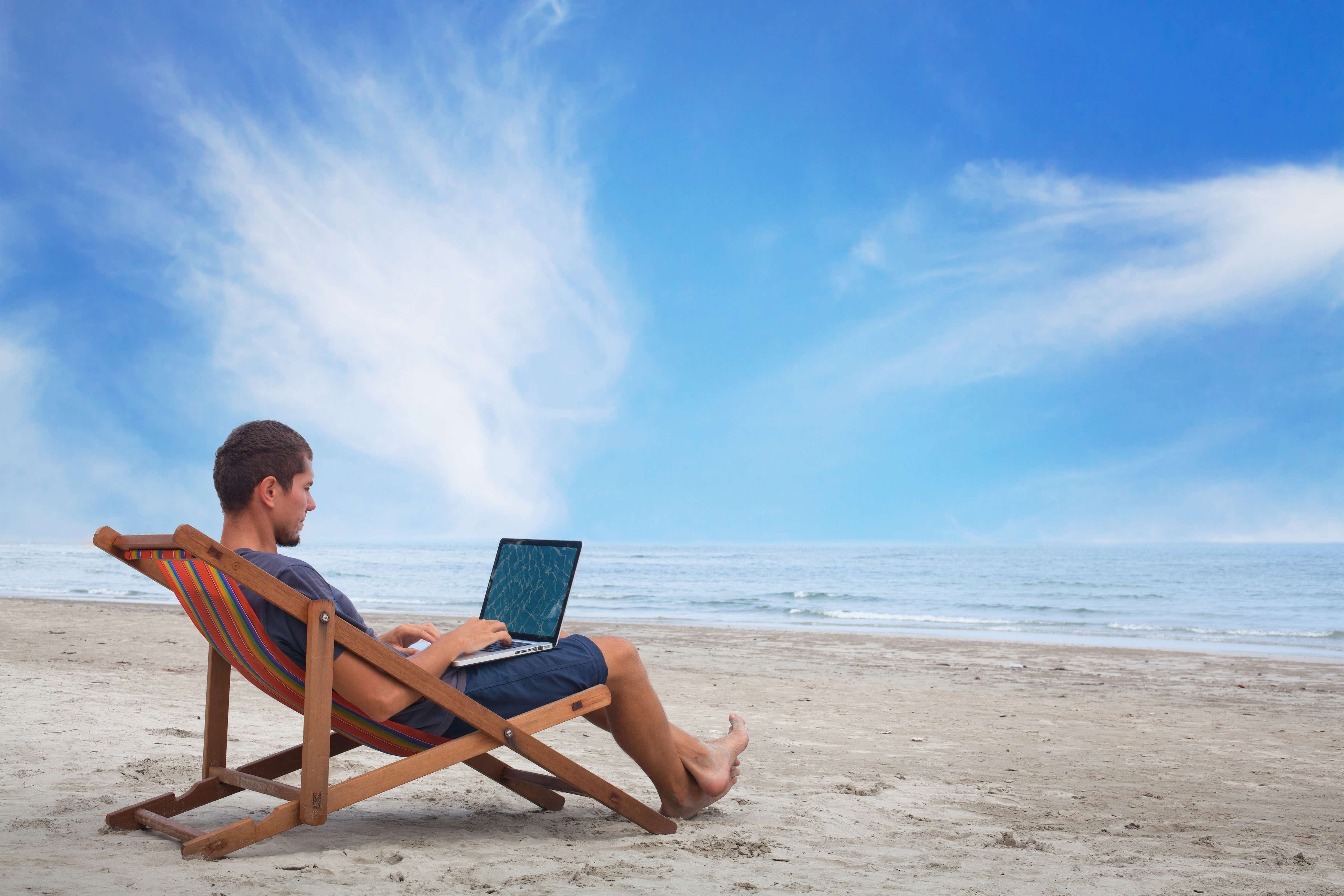 A businessman works on his laptop on a sunny day at the beach