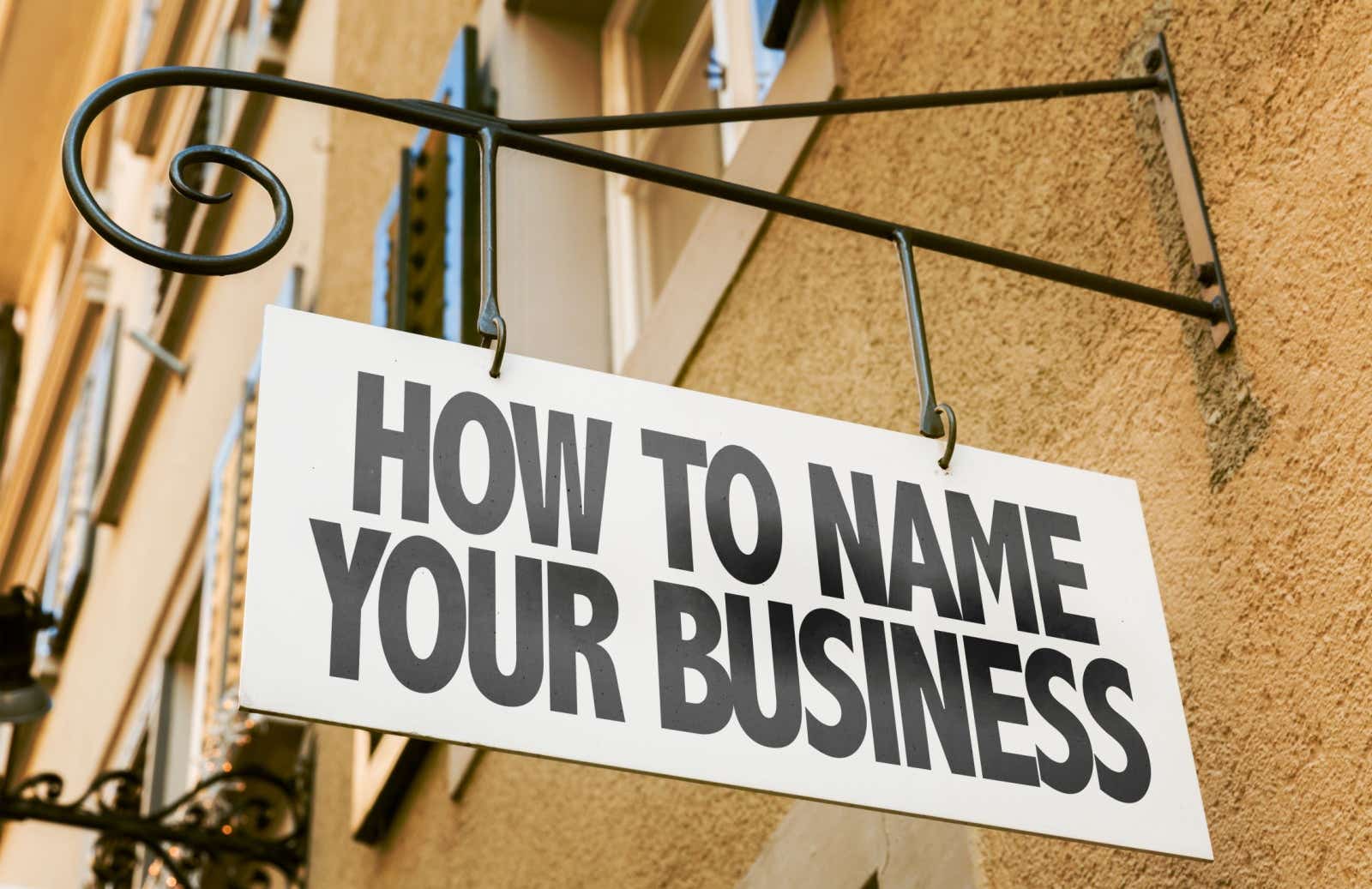 A sign hanging from a building wall saying "How to name your business".