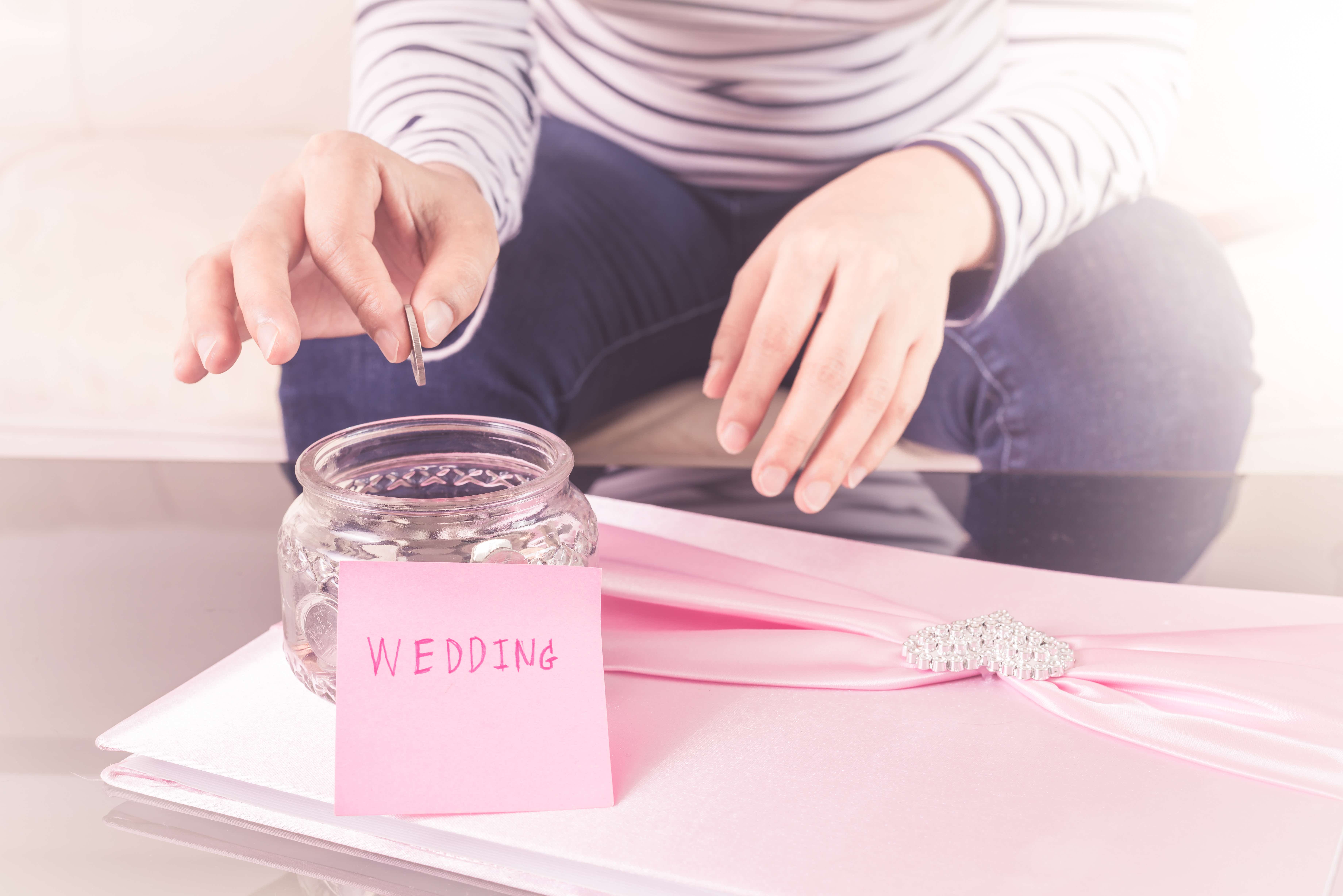 Person dropping a coin into a jar to save for a wedding