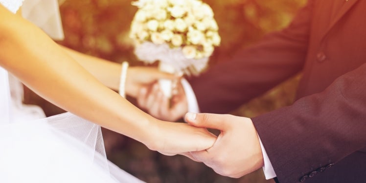 A woman holding her wedding bouquet and her new husband's hands