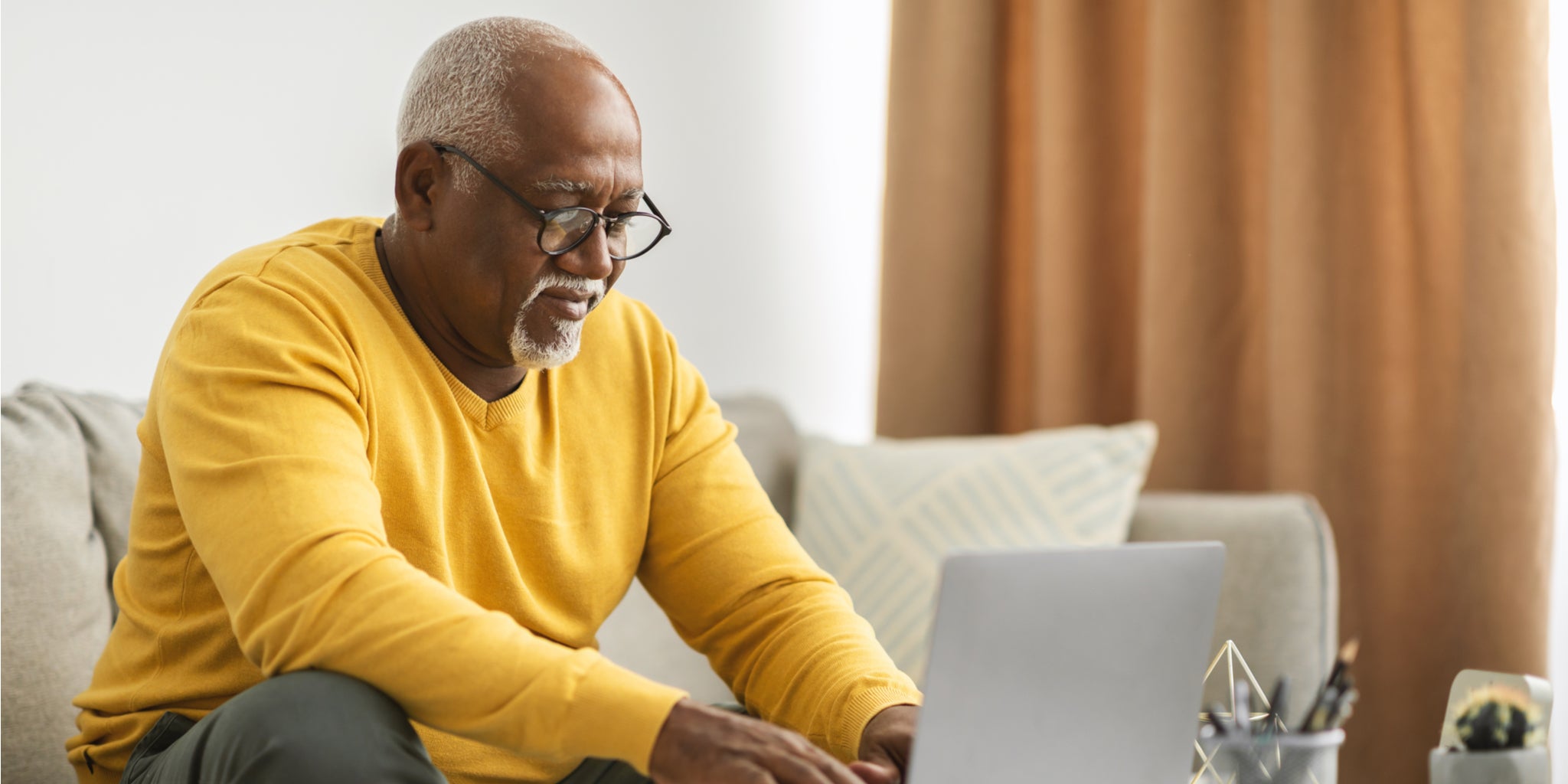 Older man, sitting on sofa working on laptop