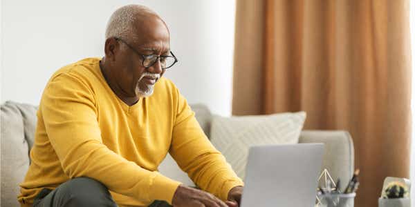 Older man, sitting on sofa working on laptop