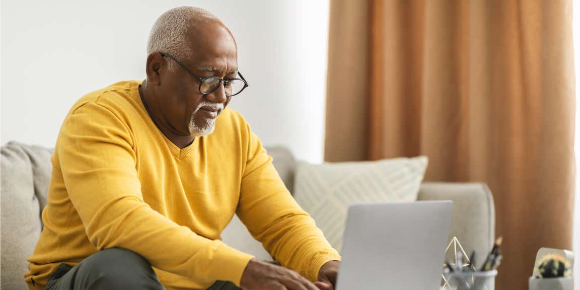 Older man, sitting on sofa working on laptop