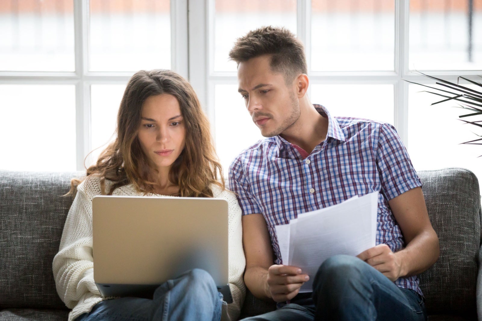 Two colleagues discuss their work while sitting on a sofa and looking at a shared laptop.