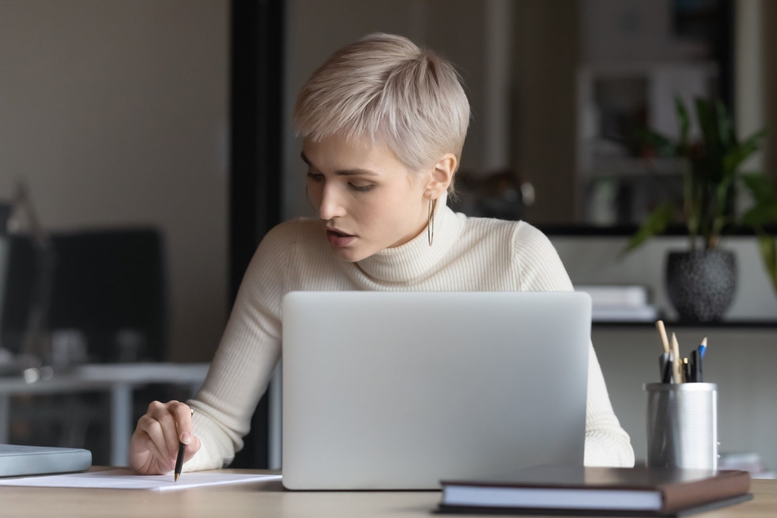 Woman working on a laptop scrutinising paperwork.