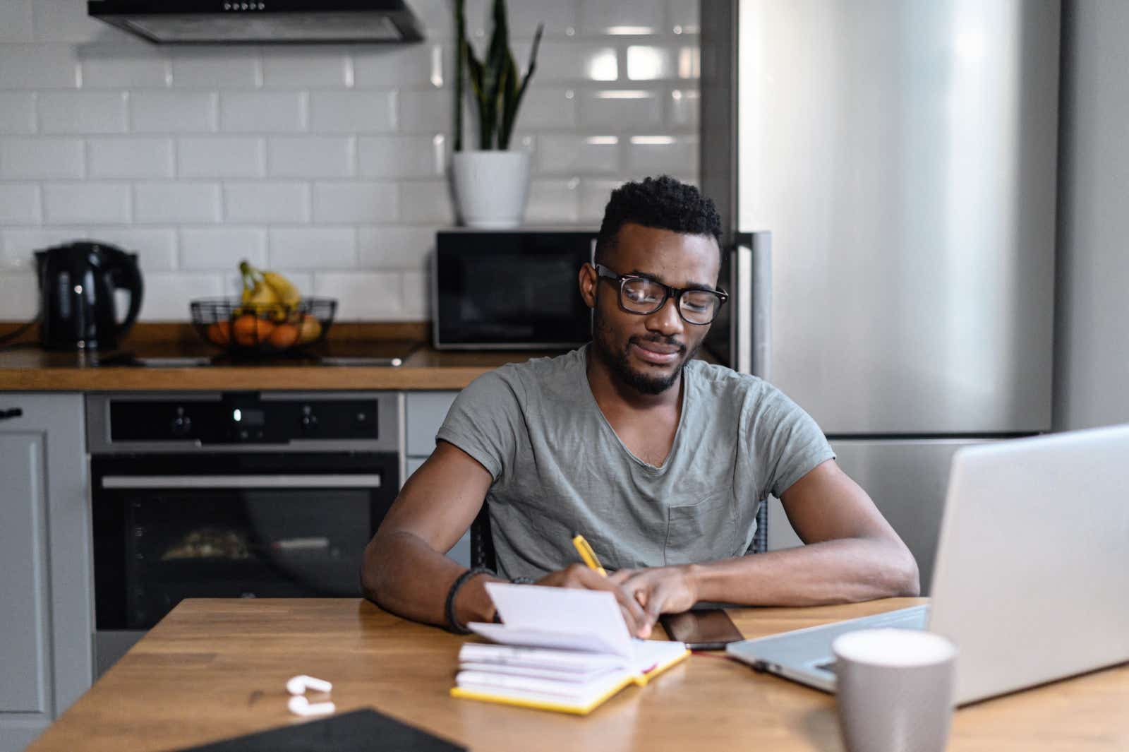 Man sitting at kitchen table with his laptop and notepad.