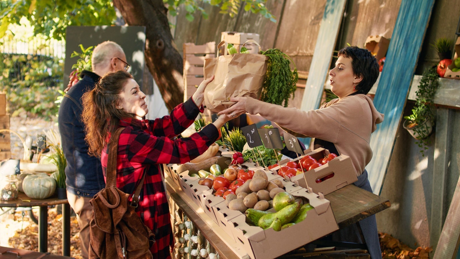 Woman handing over a paper bag of veg to a customer at a fruit and veg stall