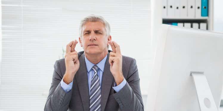 businessman-sat-at-desk-with-fingers-crossed