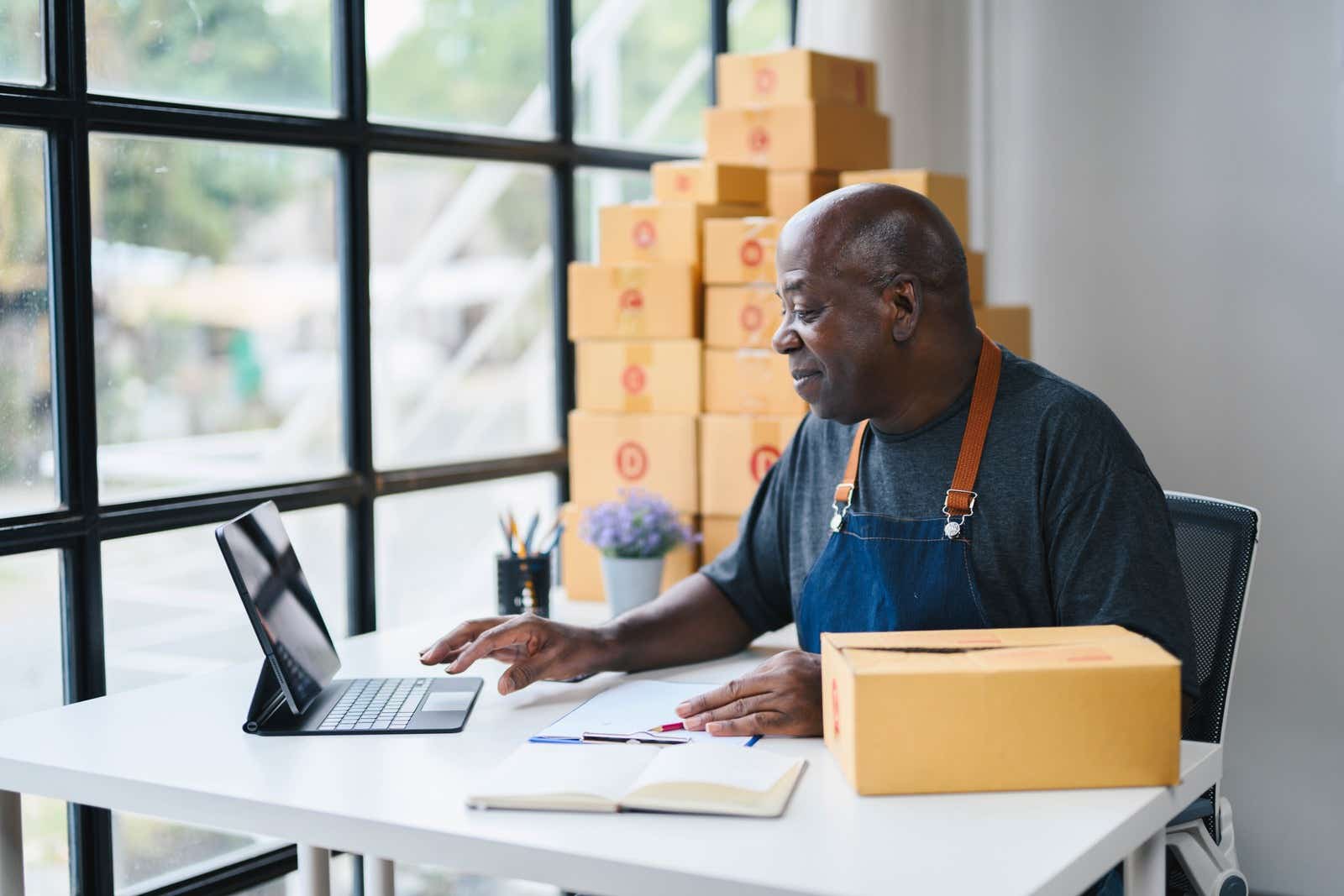 Senior man working on a tablet in a home office surrounded by cardboard boxes