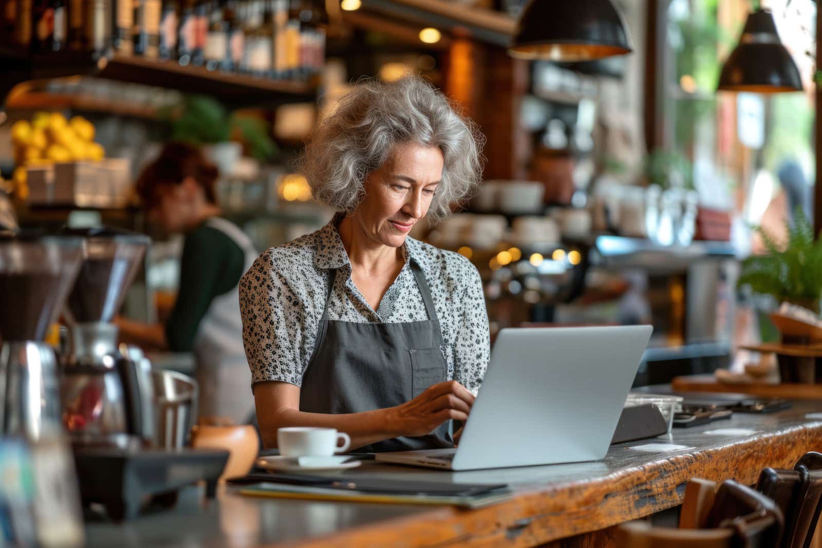 Small business owner working with a laptop computer behind the counter of a cafe.