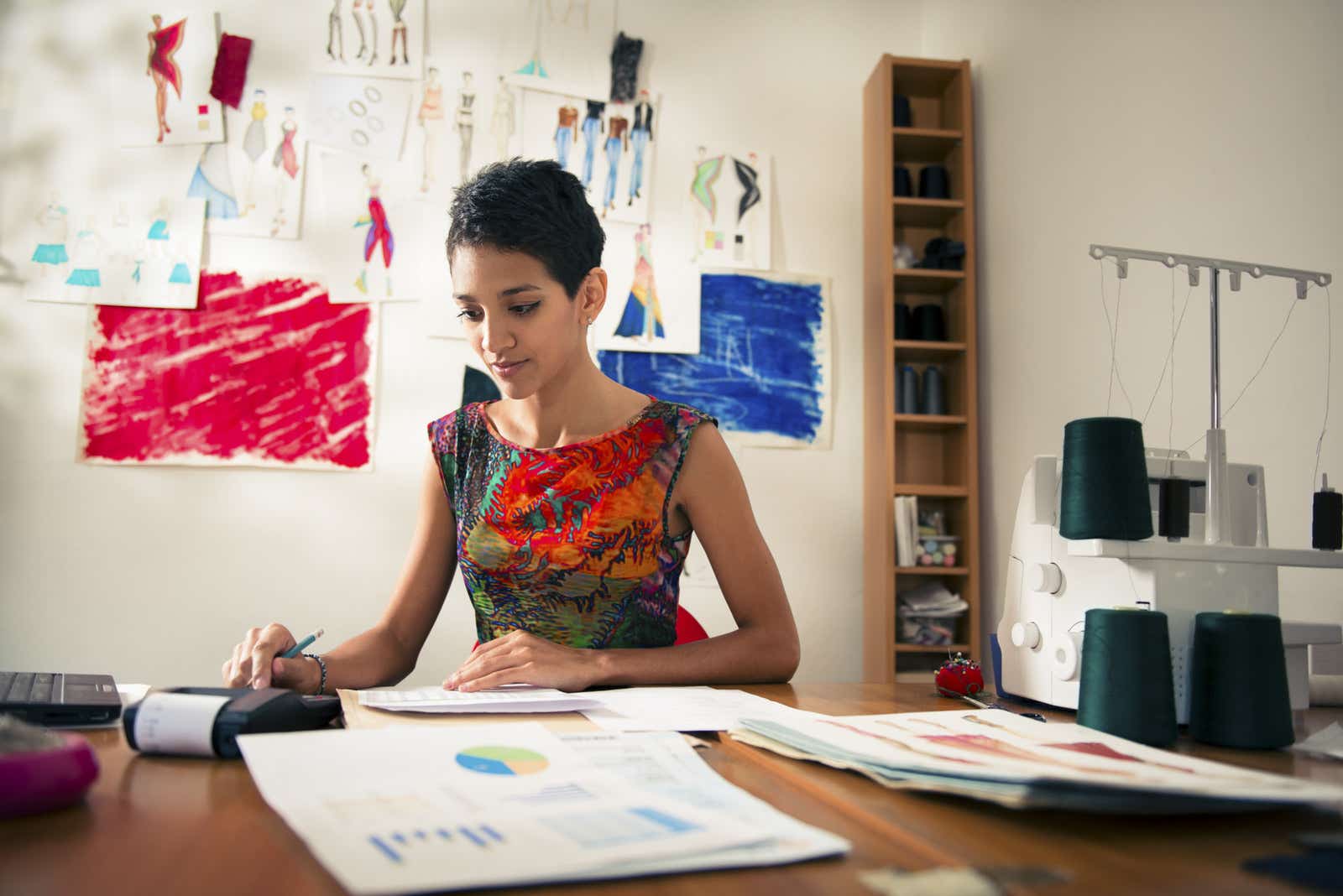 Self-employed woman with calculator, computer and papers in a fashion design studio