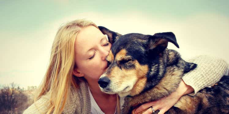 Woman kissing a dog on the head outside.