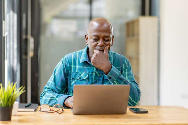A businessman working on a laptop, considering what's on his screen.