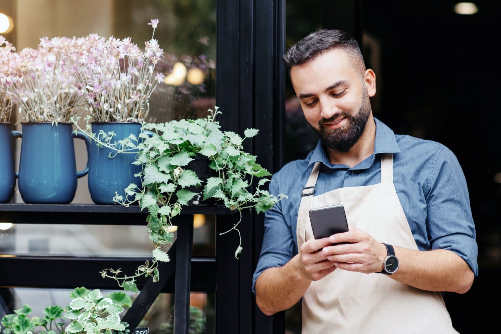 Businessman leaning on his shop doorway while looking at his smartphone.