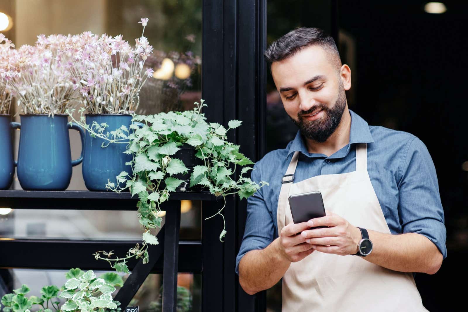 Businessman leaning on his shop doorway while looking at his smartphone.