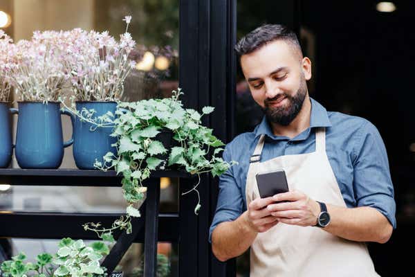 Businessman leaning on his shop doorway while looking at his smartphone.
