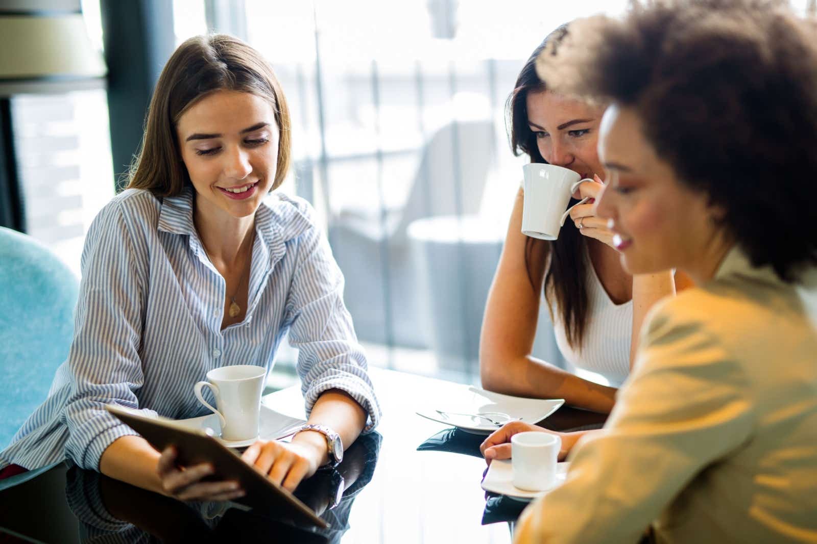 Group of woman looking at a shared tablet while drinking coffee.