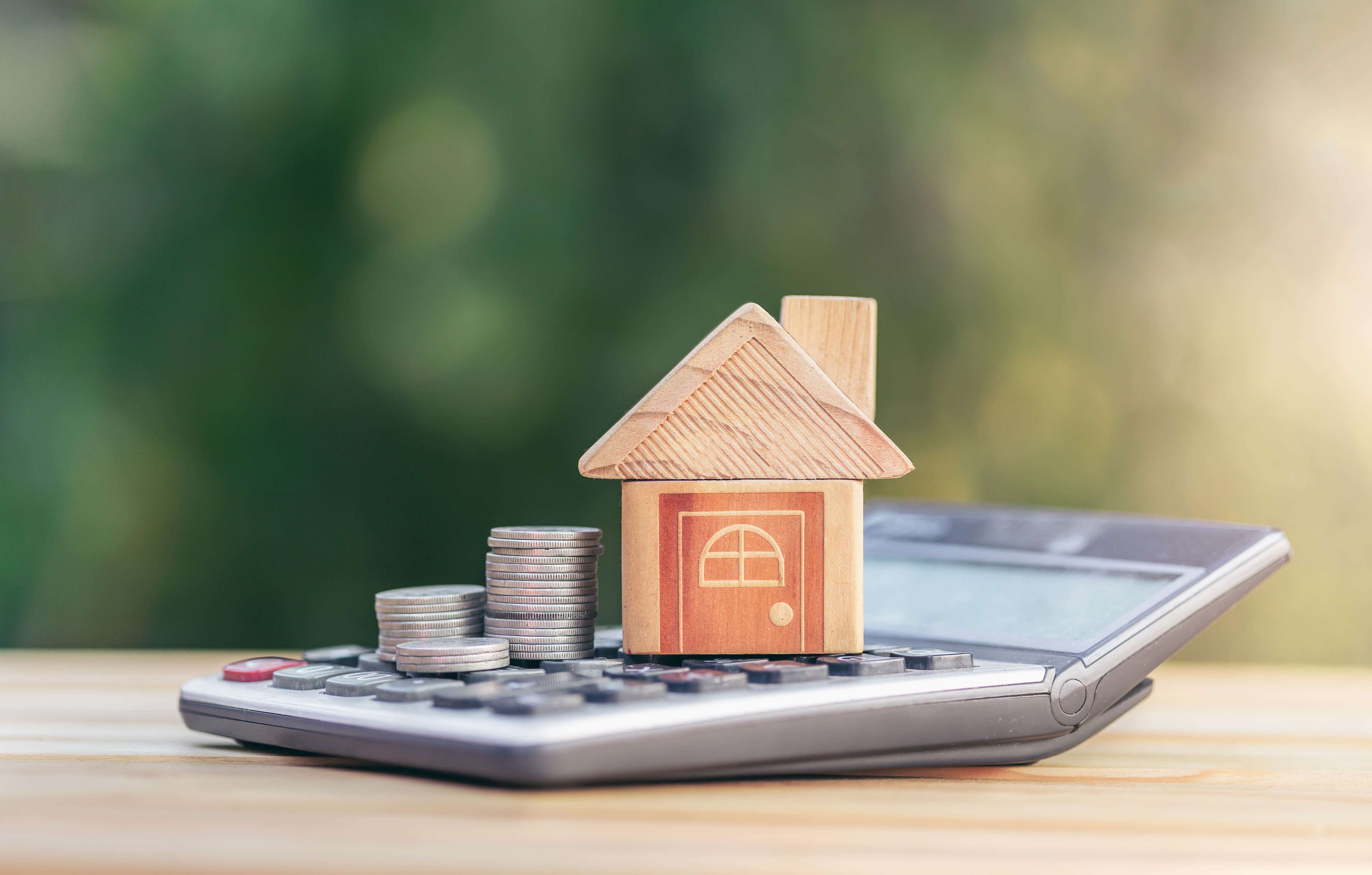 A calculator with a model house and coins on top of it.