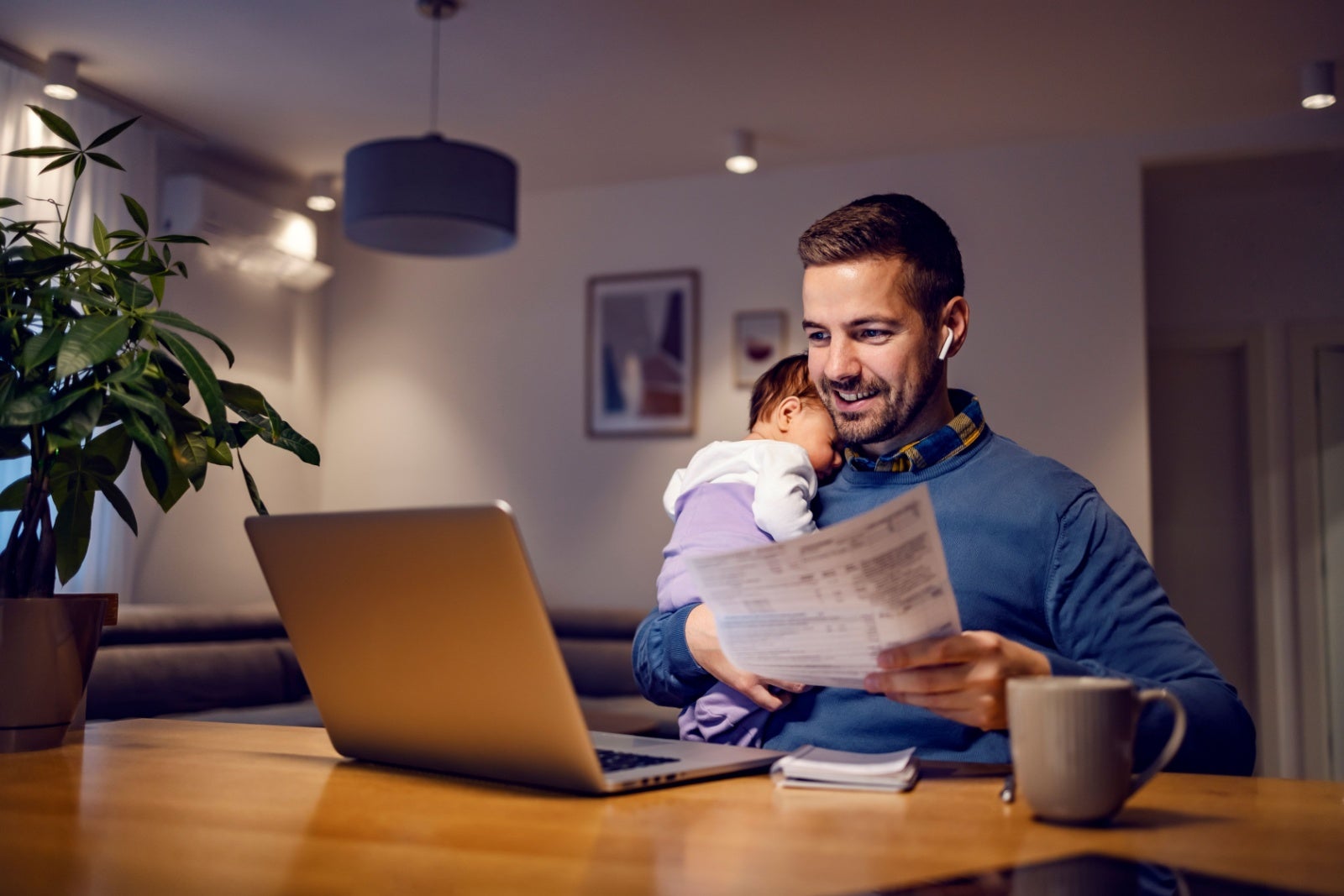 Small business owner with paperwork and a sleeping baby on his shoulder.