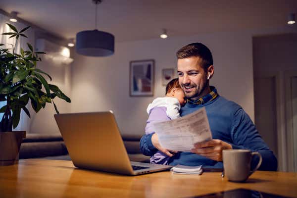 Small business owner with paperwork and a sleeping baby on his shoulder.