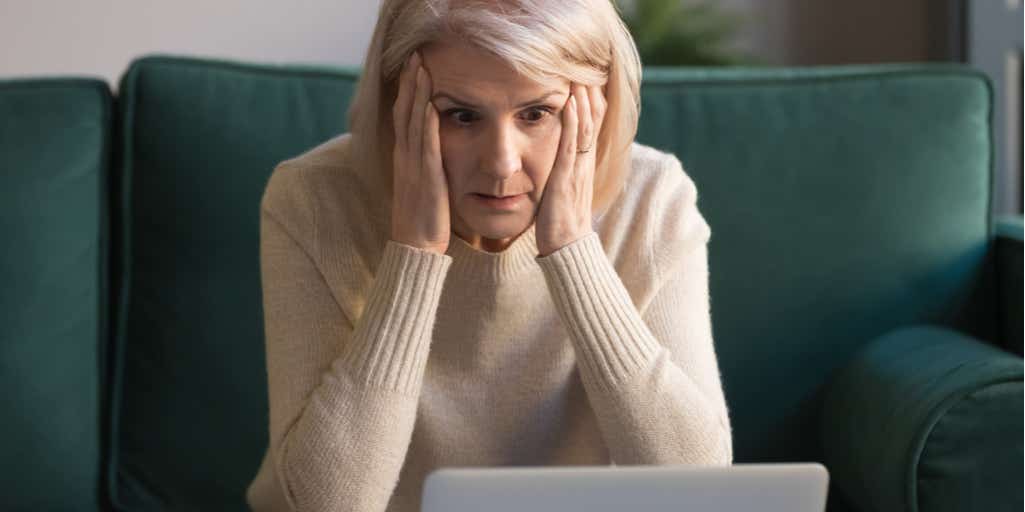 photograph of a middle aged woman looking shocked with head in hands.