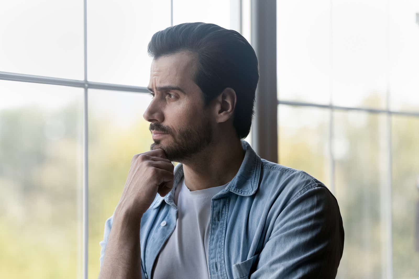 Pensive millennial business owner standing by a window and contemplating business finances