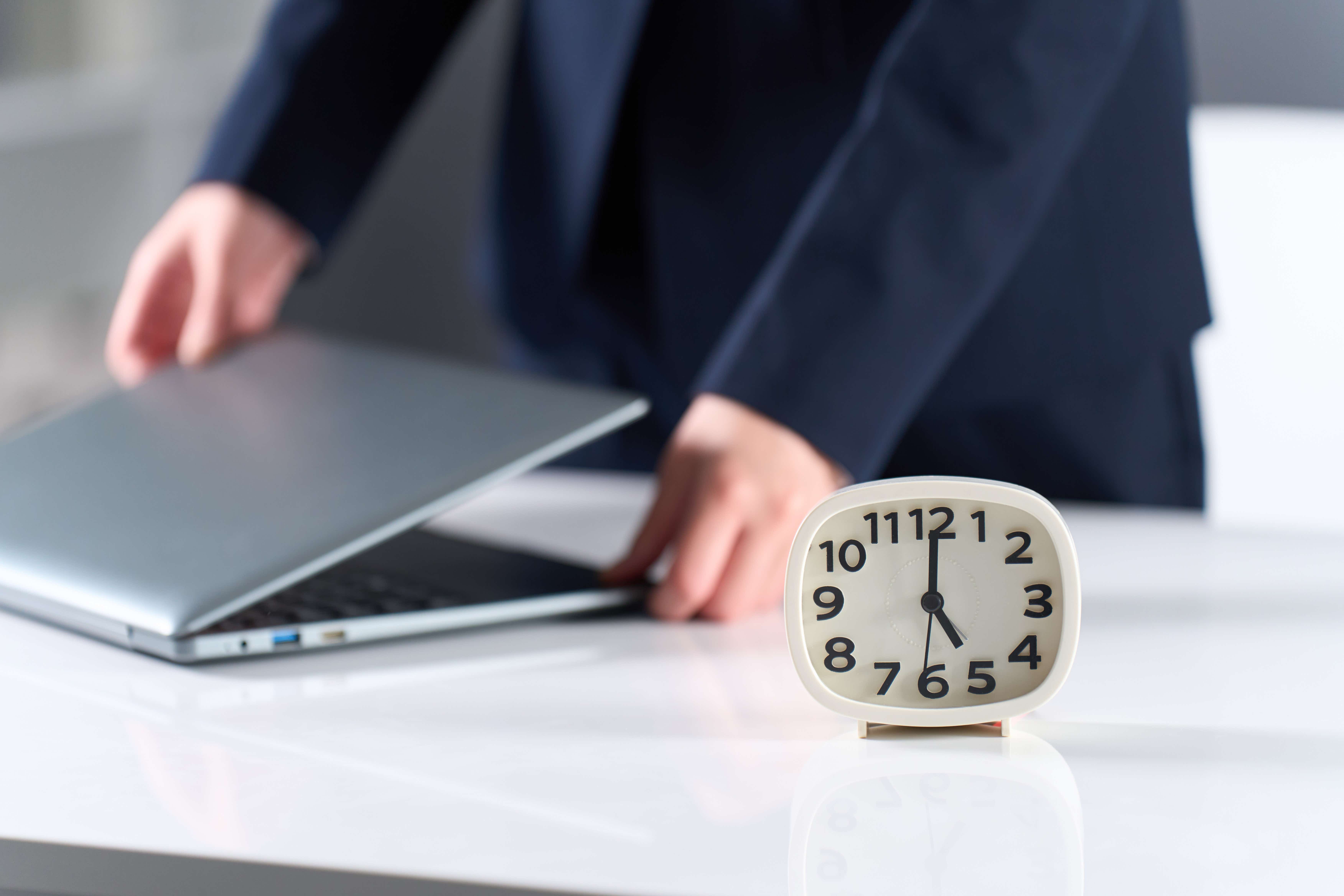 A worker closes their laptop as a clock displays 5pm