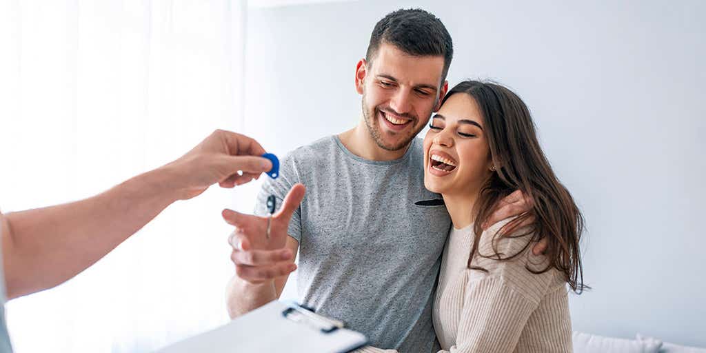 Young couple taking keys of their new house from broker.