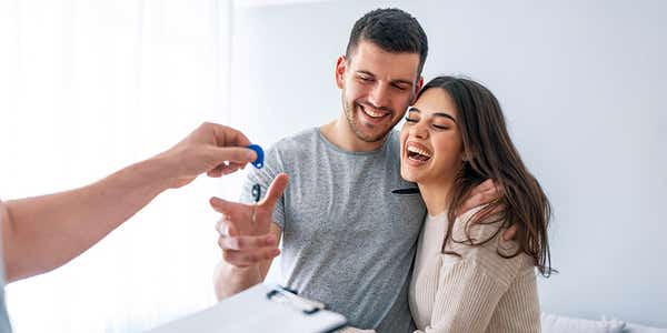 Young couple taking keys of their new house from broker.