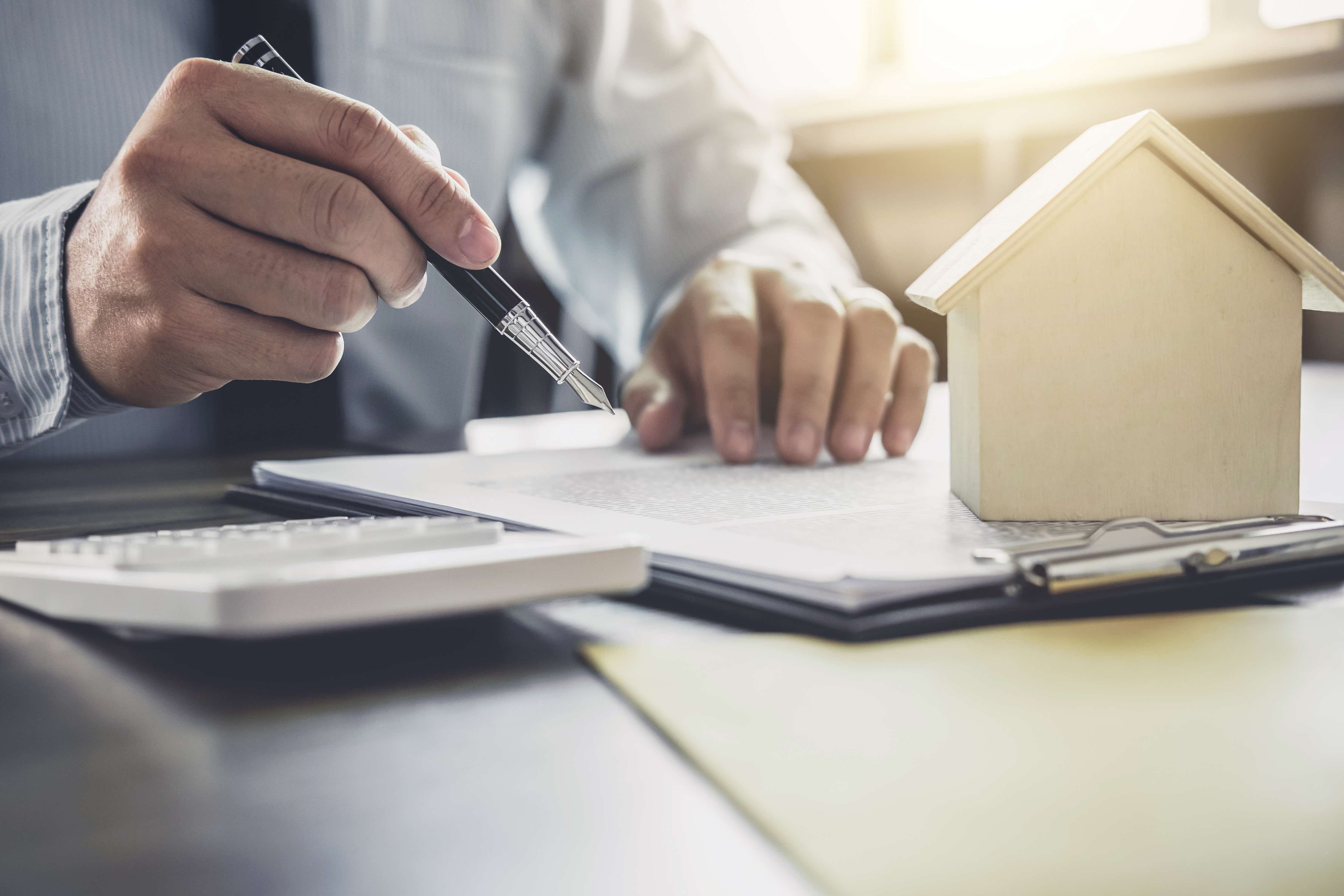 Image of a person doing paperwork with a model of a house on their clipboard.