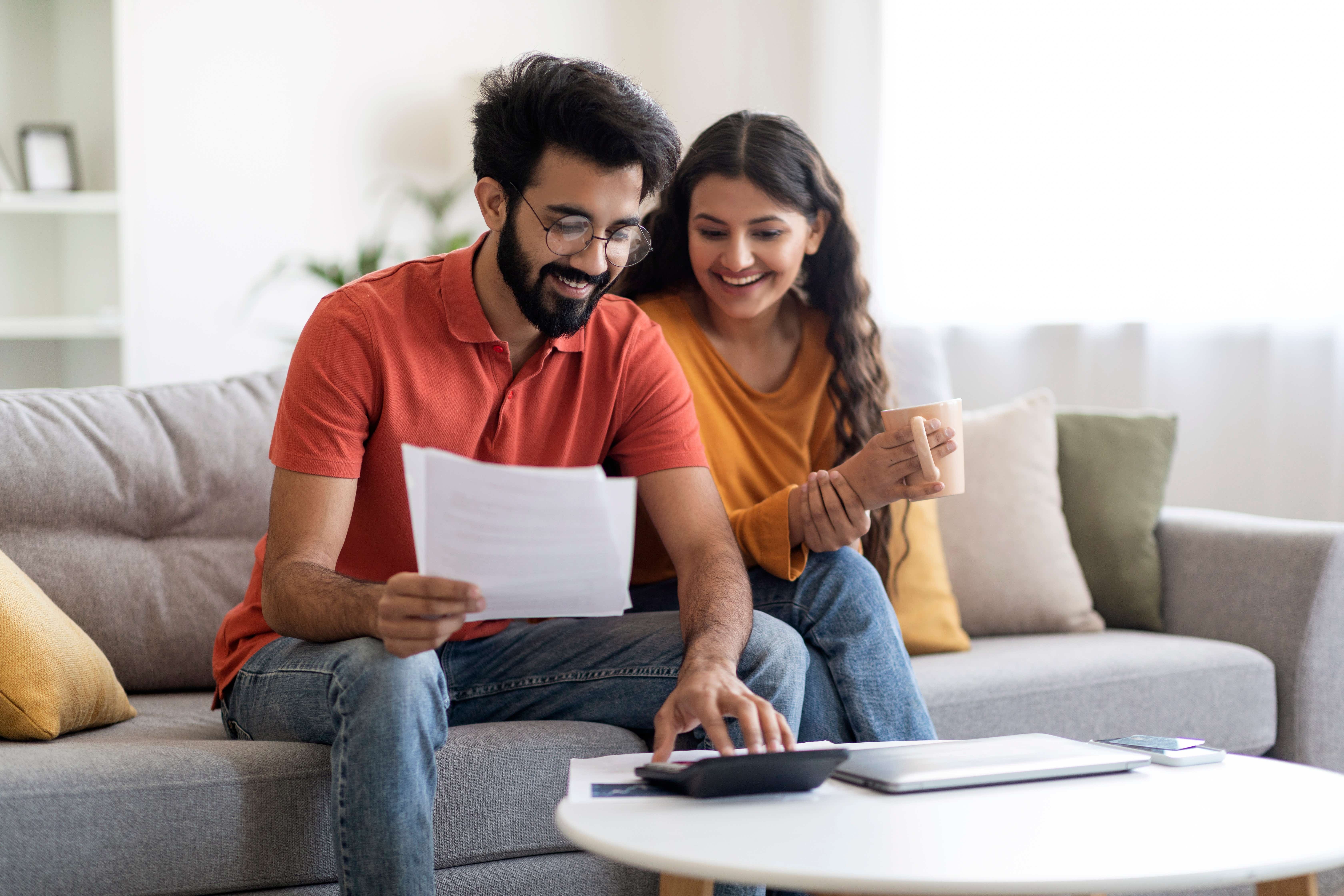 Couple sitting on a sofa looking at a calculator and holding pieces of paper