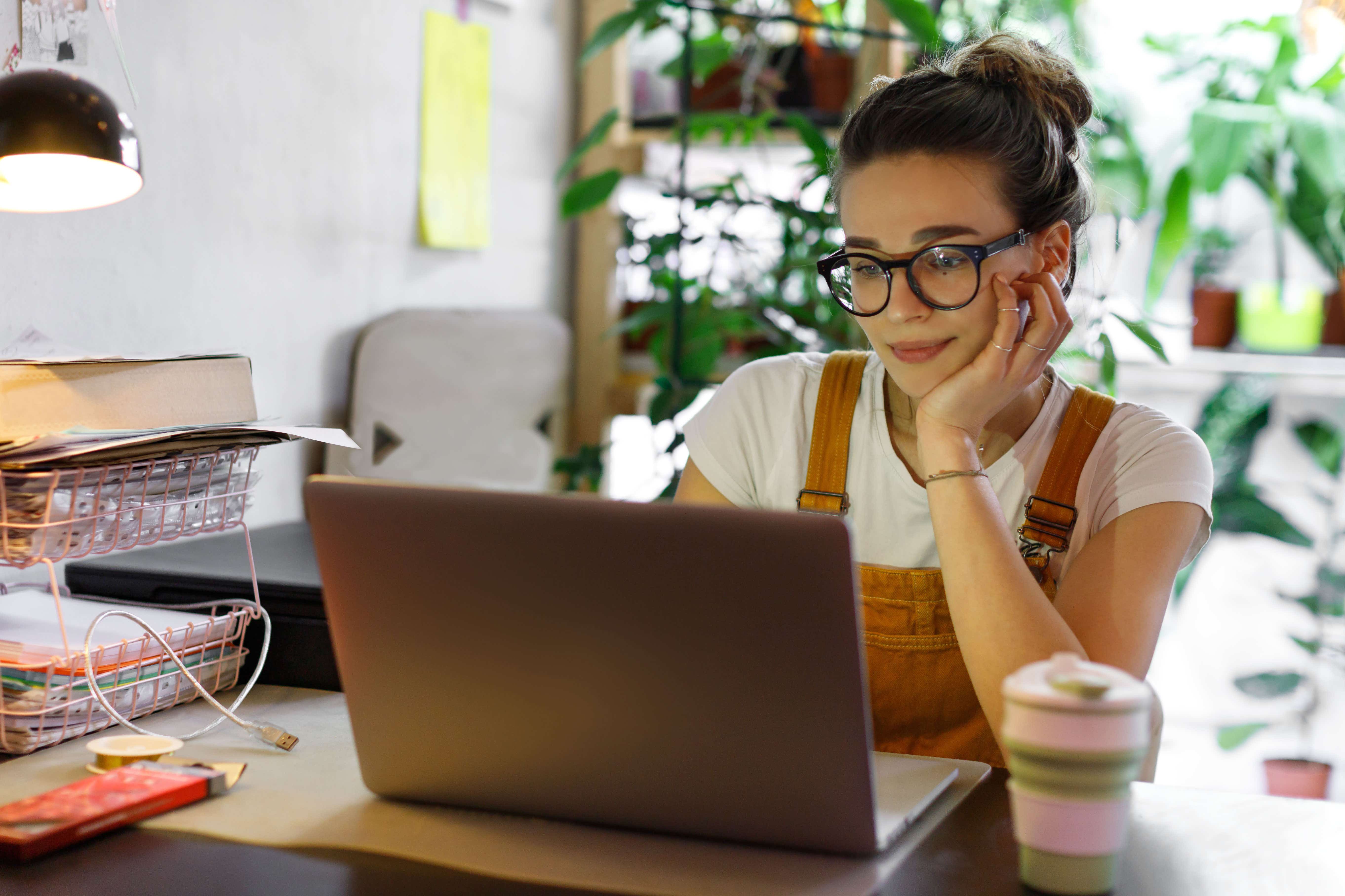 Female entrepreneur working on a laptop, surrounded by plants and office supplies.