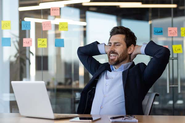 A smiling businessman leaning back in his seat with his hands behind his head. 