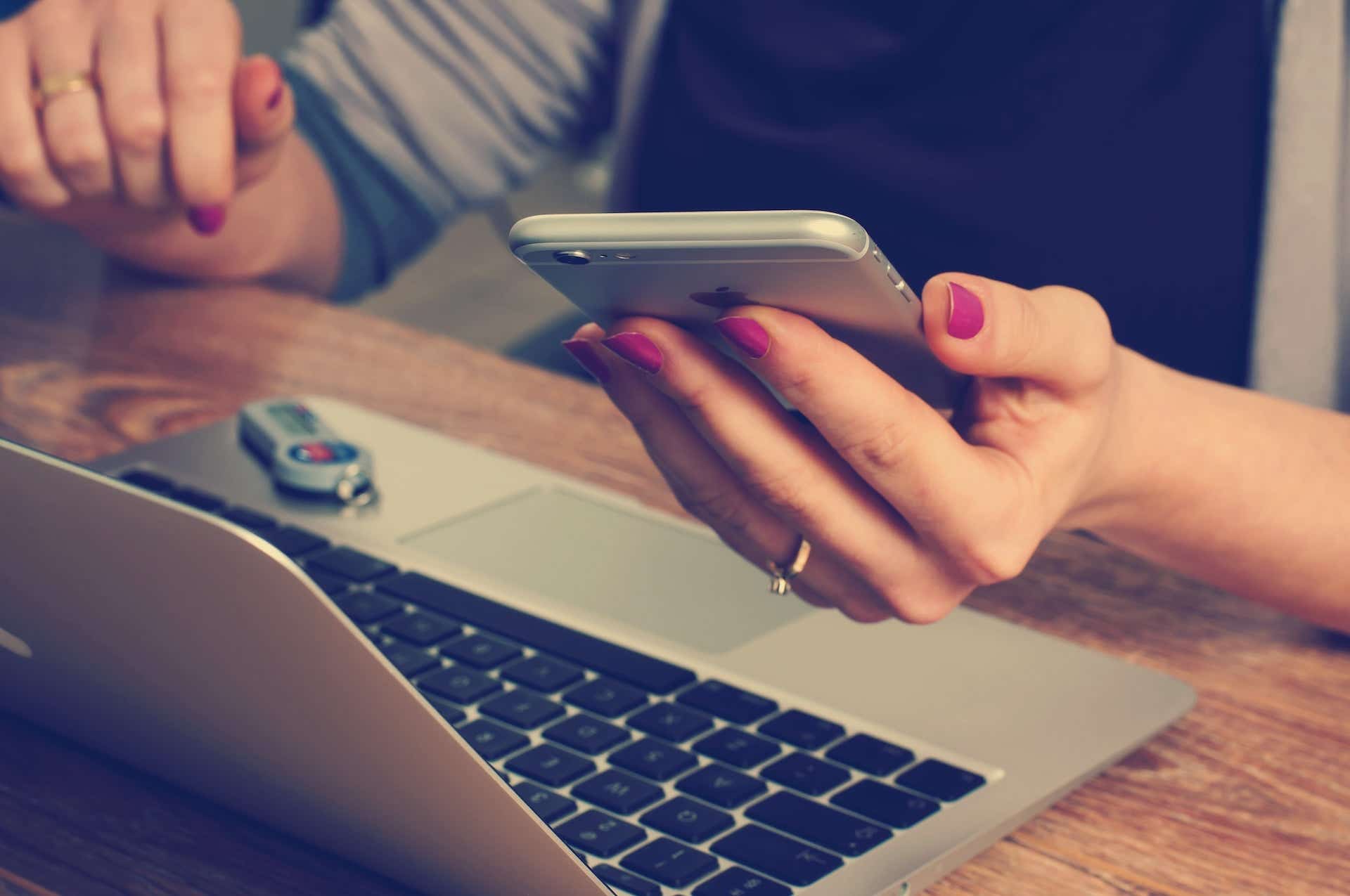 Woman holding phone and sitting at a laptop