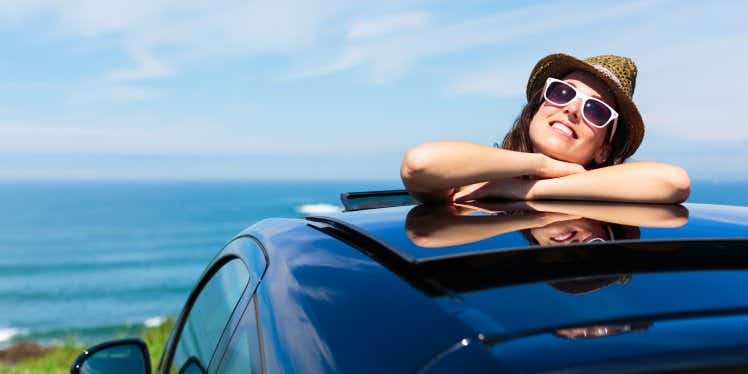 Woman sticking her head out of her car's sun roof by the sea