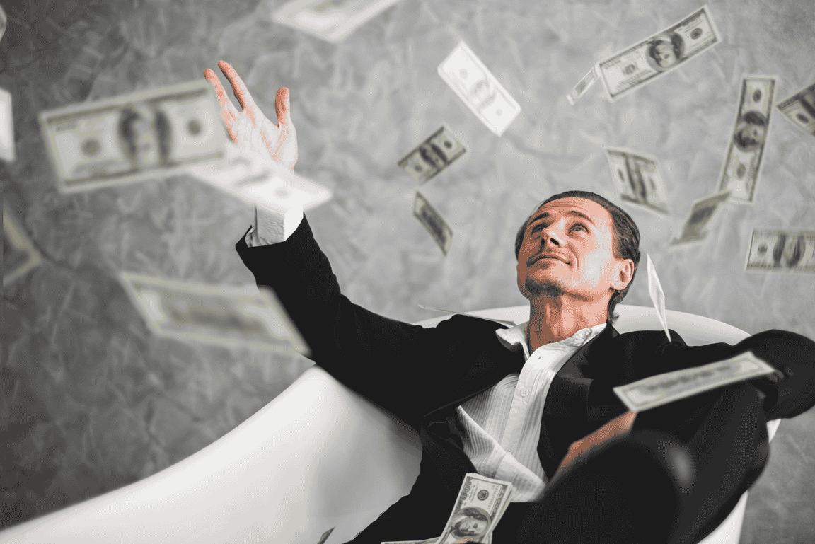 Fully-dressed man in an empty bath with money raining down on him