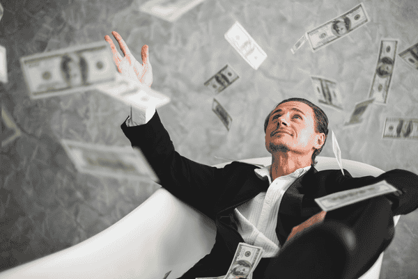Fully-dressed man in an empty bath with money raining down on him