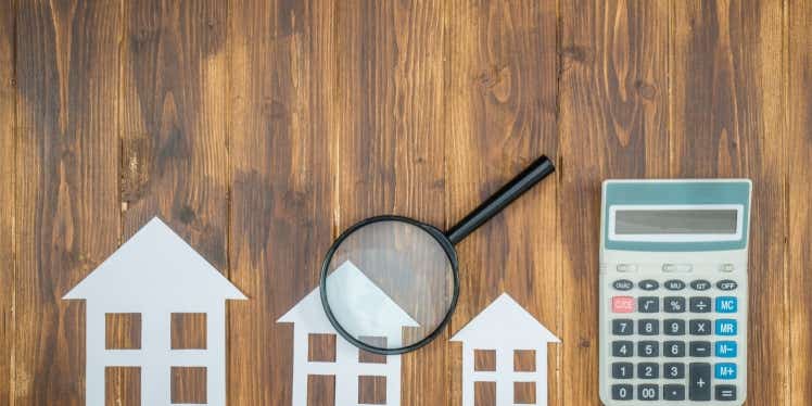 Paper houses, a magnifying glass and a calculator on a table looking down from above.