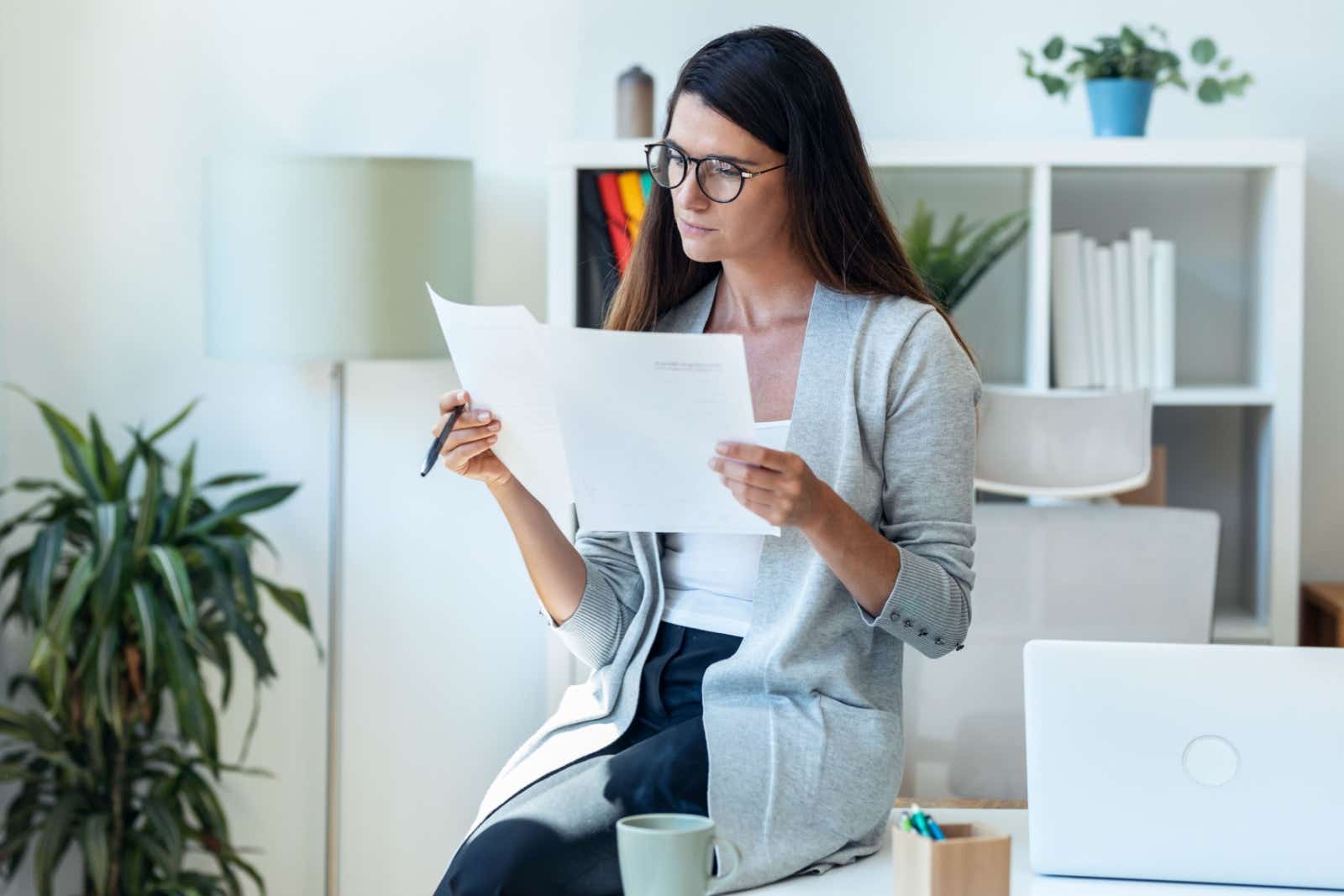 Casually dressed businesswoman sitting on her desk studying paperwork