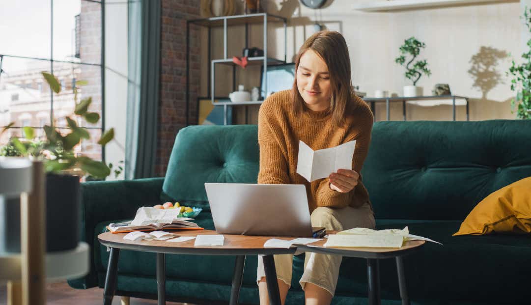 Freelancer reviewing tax documents on laptop at home with piles of receipts on table