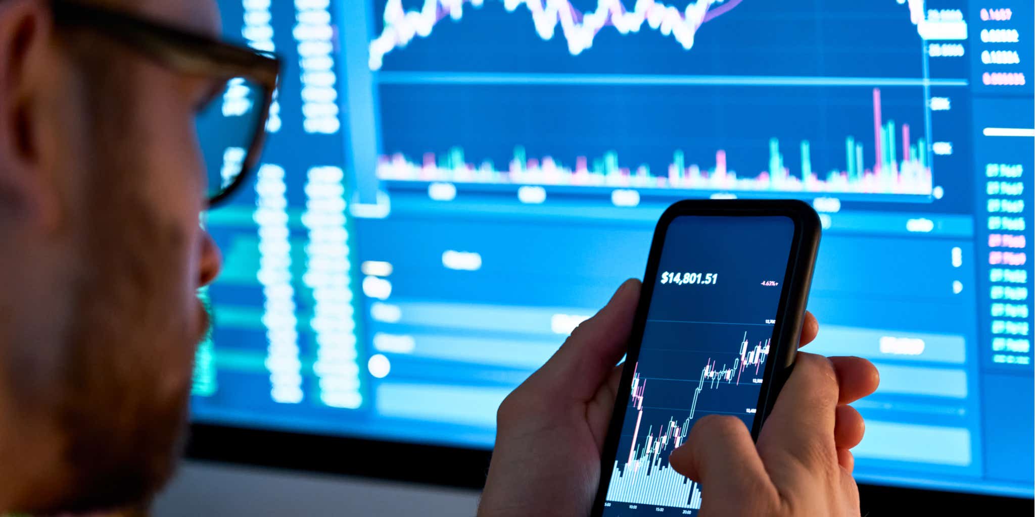 Man investing using mobile phone and large monitor