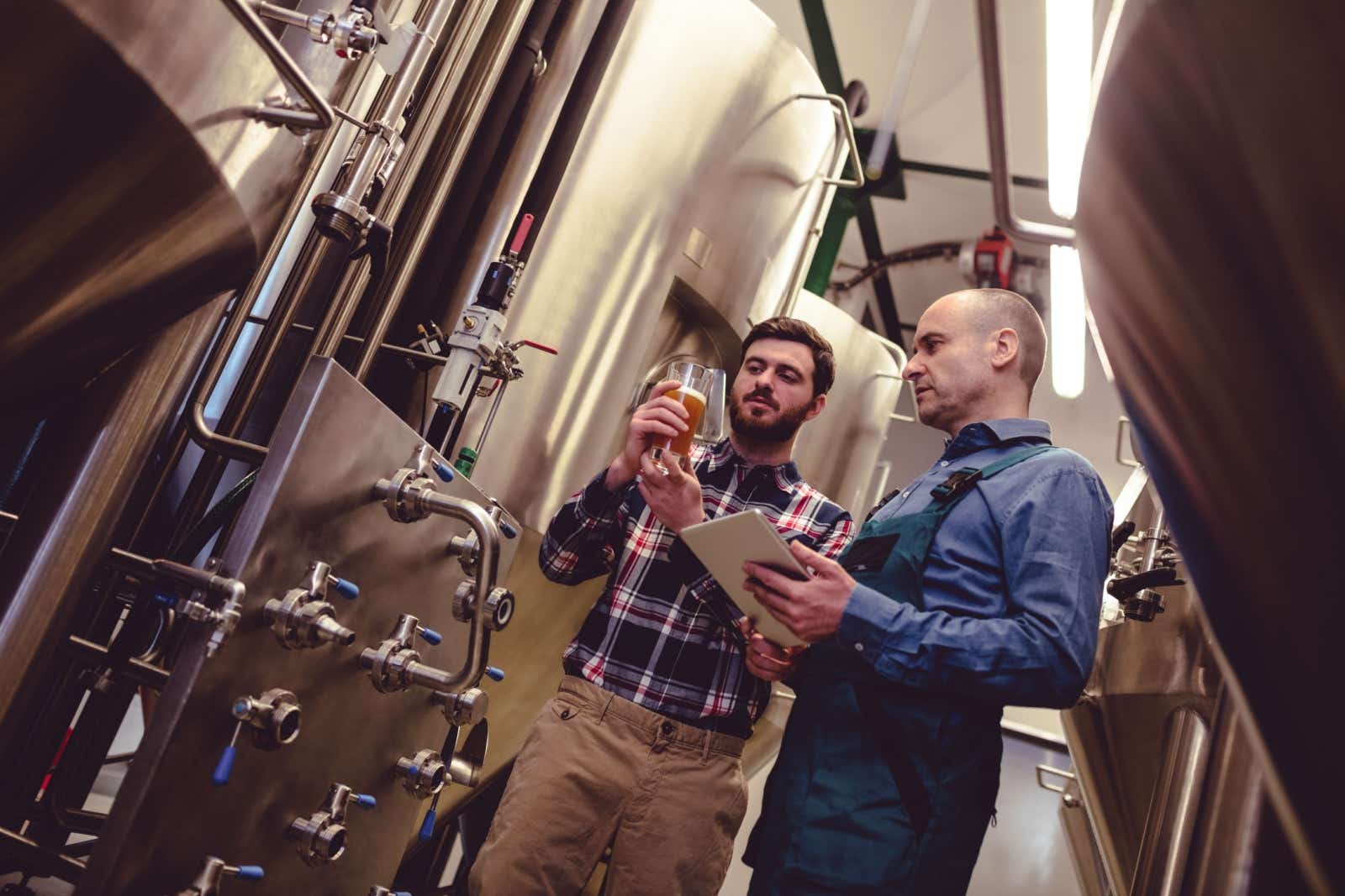 Two workers surrounded by large stainless steel vats at a microbrewery.