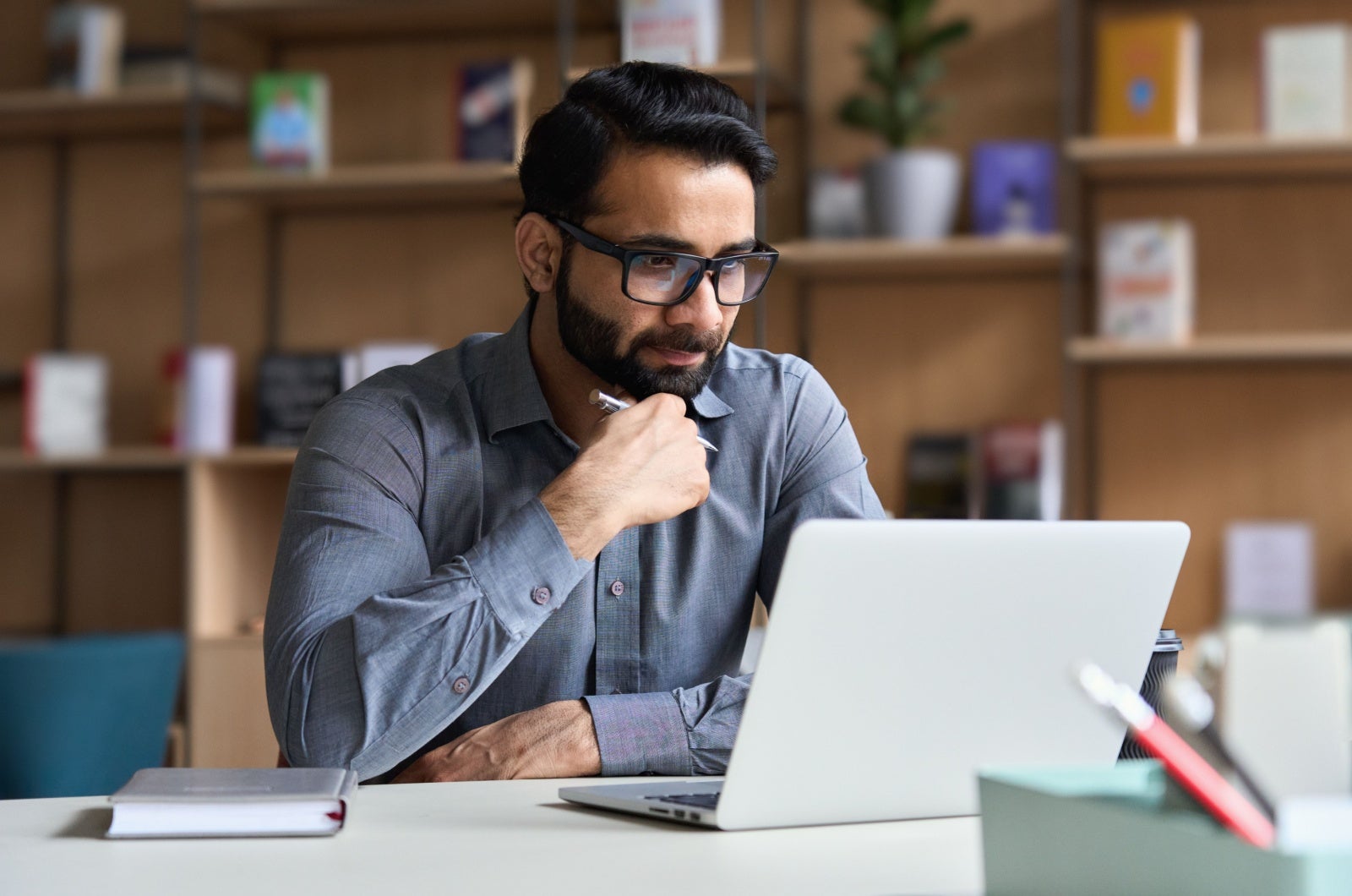 Businessman working on his laptop in an office with wooden shelves.