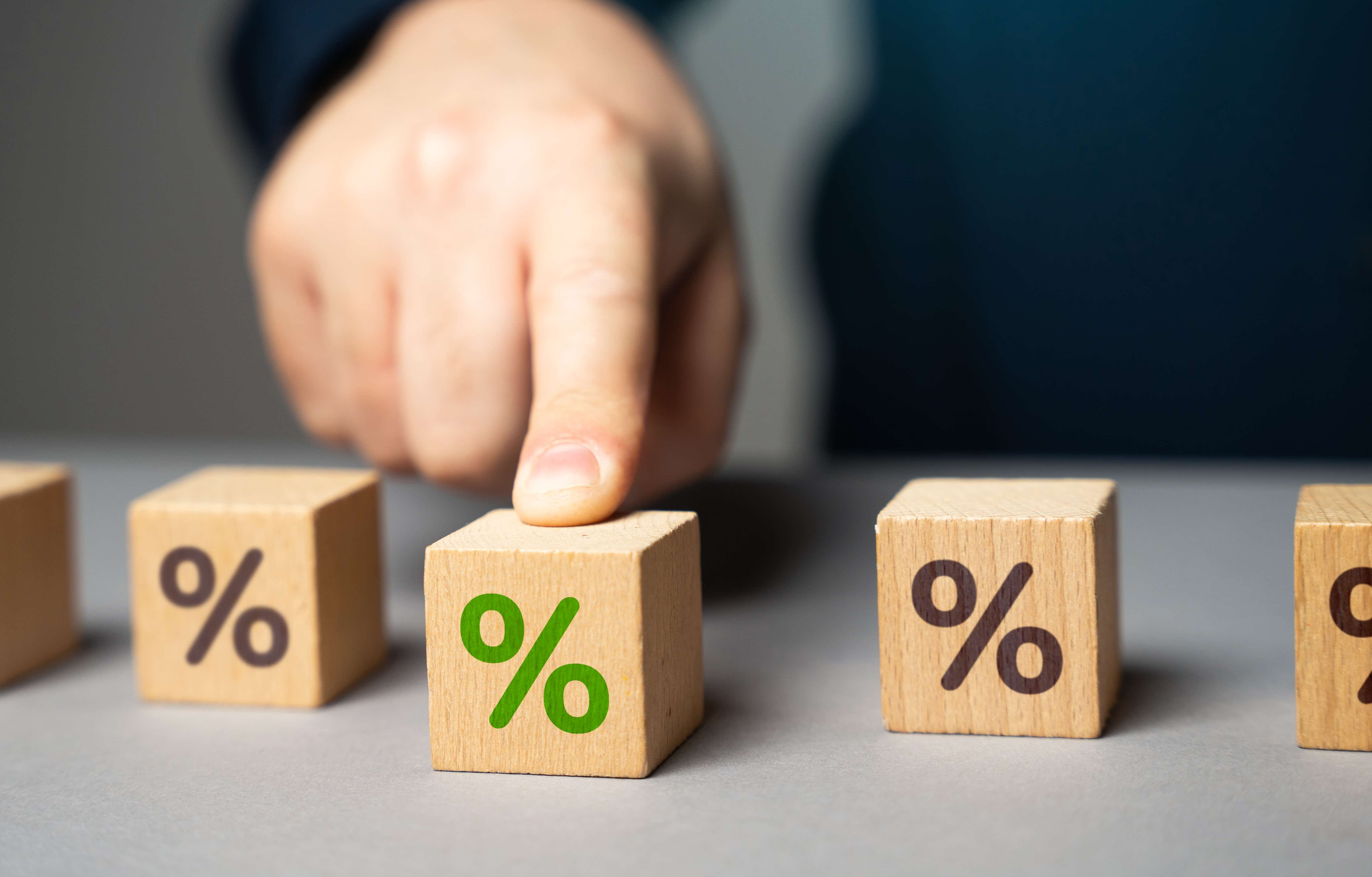 Three wooden blocks with percentage symbol, one is green and has a man's finger on it. 