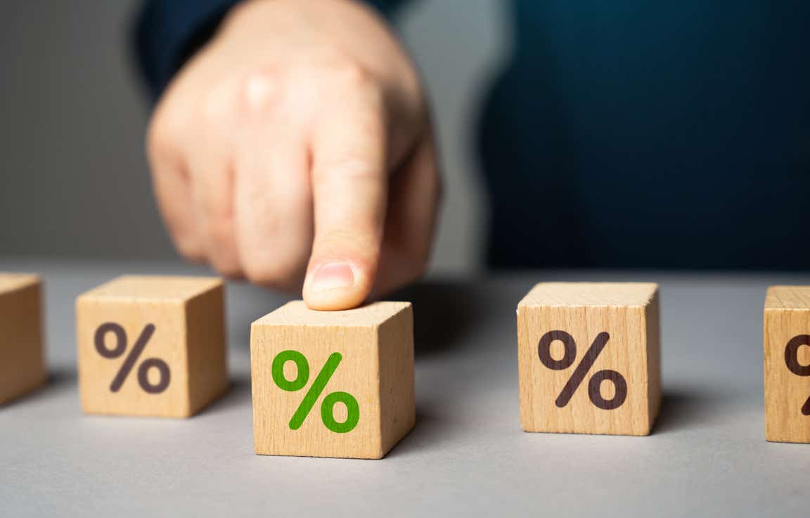 Three wooden blocks with percentage symbol, one is green and has a man's finger on it.