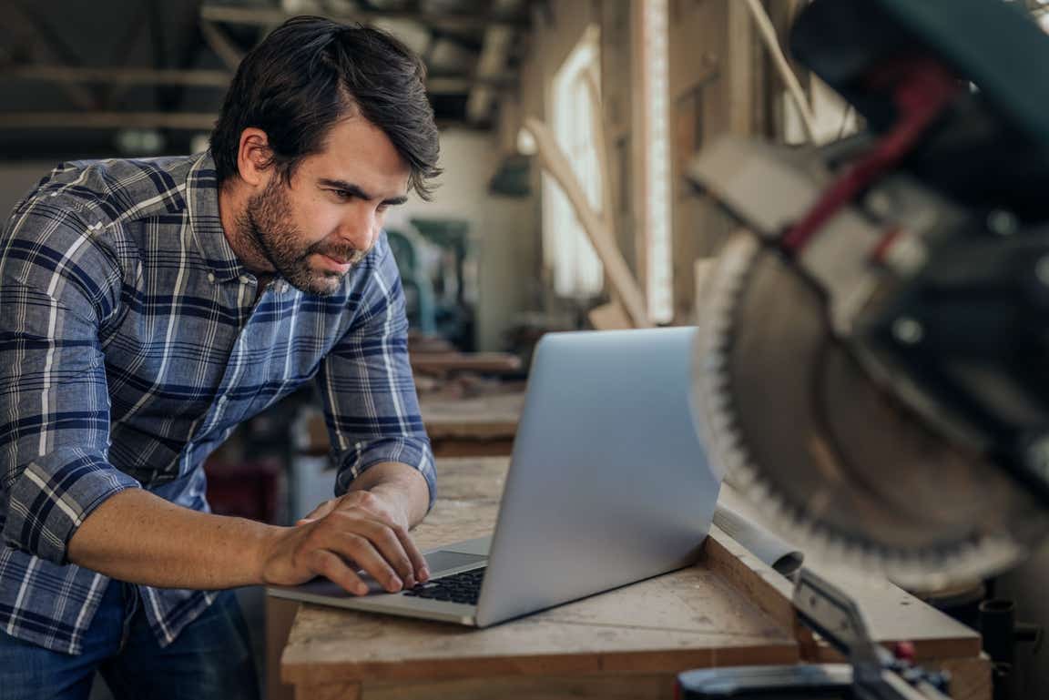 Business man working on his laptop in his joinery workshop.