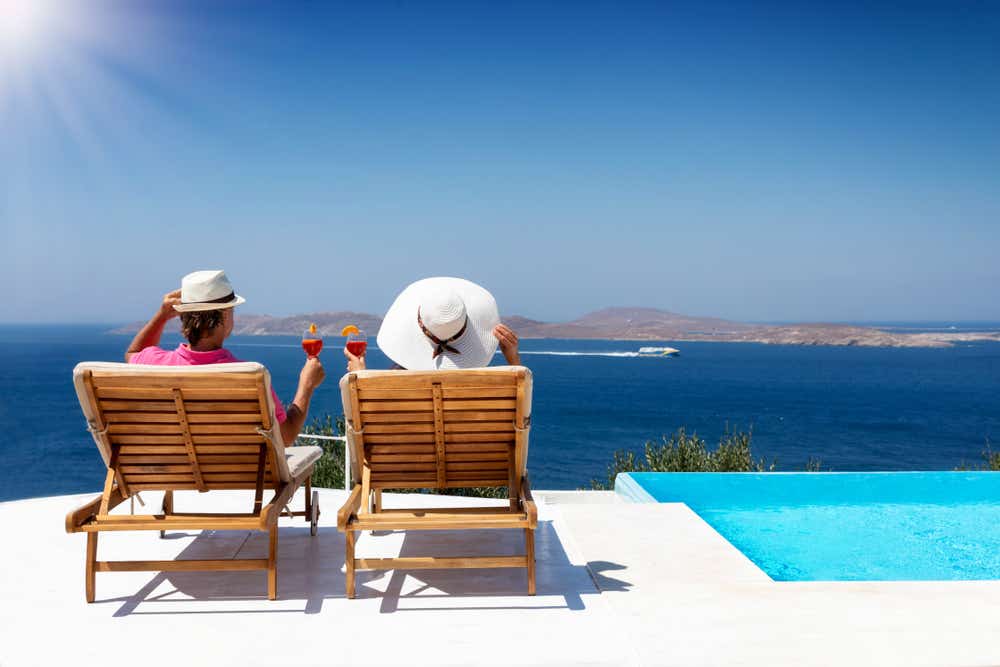 A couple are on holiday sitting in deck chairs and admiring the sea view. 