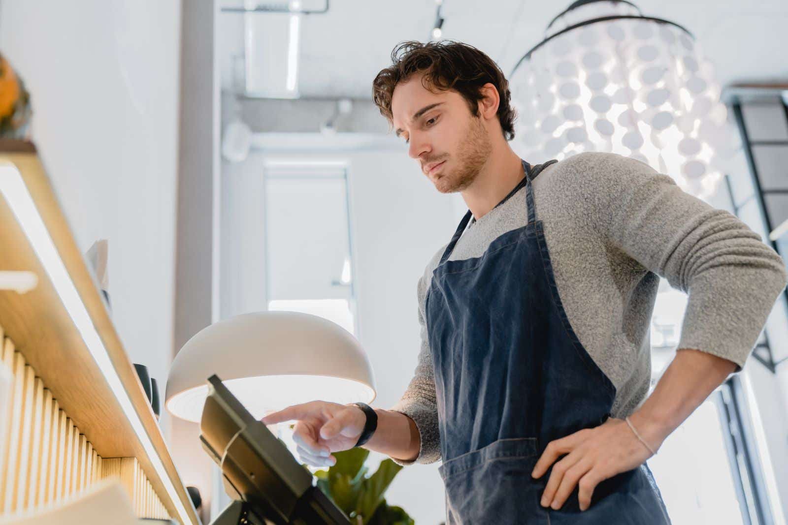 A man in an apron works a digital till.